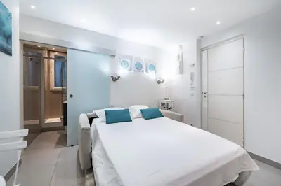a white bedroom with a large bed with blue pillows at Appartement Studio idéalement situé - Palais Miramar in Cannes