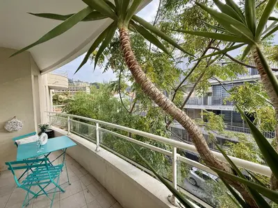a balcony with a blue table and a palm tree at DAPHNE, appartement piscine in Cannes