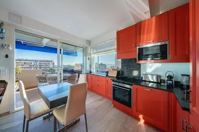 a kitchen with red cabinets and a table and a dining room at COZYSTAY - Charmant 3 pièces en dernier étage in Cannes