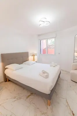 a white bedroom with a large bed and a window at Rez-de-Jardin à Cannes Centre - Luxe & Design in Cannes