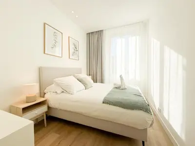 a white bedroom with a bed and a window at The Cosy Clémenceau in Cannes