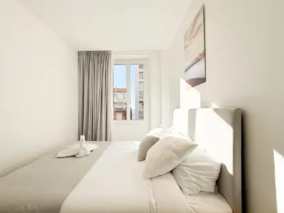 a white bedroom with a bed with a window at The Cosy Clémenceau in Cannes