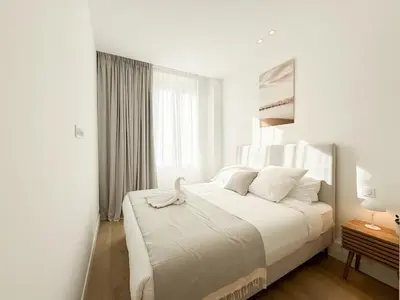a white bedroom with a large bed with white sheets at The Cosy Clémenceau in Cannes