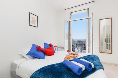 a white bedroom with a large bed with blue pillows at BnGo l Ruby Suite l 2ch, 7p, vue mer, centre in Cannes