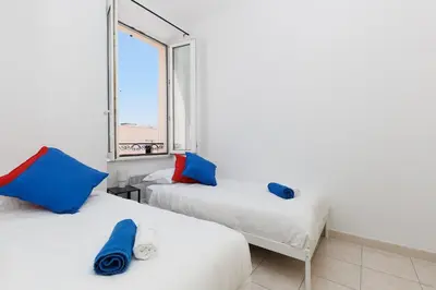 two beds with blue and red pillows in a room with a window at BnGo l Amber Suite l 2ch, 6 personnes, centre in Cannes