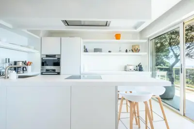 a white kitchen with white cabinets and stools at Résidence 3p, Terrasse Aménagée, Piscine, Vue Sur Les îles - 3P, terrasse aménagée, piscine, vue sur les îles MAE-2193 in Cannes