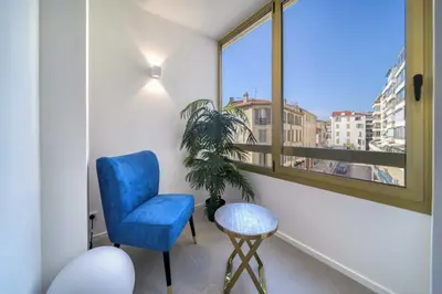 a blue chair and a table in a room with a window at REF 1295 - Cannes Croisette - Sea view apartment for rent in Cannes