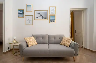 a couch in a living room with pictures on the wall at Spacious and Bright Near Train Station and Palais des Festivals - BENAKEY in Cannes