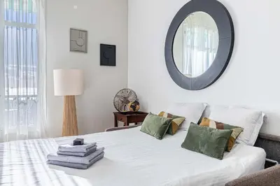 a bedroom with a white bed with a mirror on the wall at 20 LACROIX - Cozy 2-bedroom apartment with balcony and sea view in Cannes