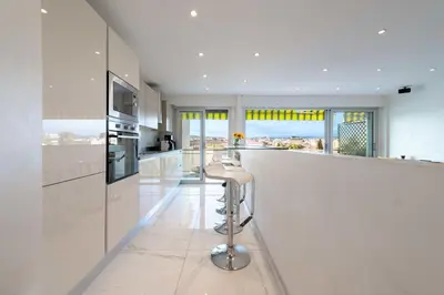 a white kitchen with a bar with stools at 1-Br Apartment with Terrace Near City Centre in Cannes