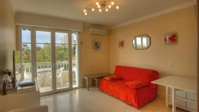 a living room with a red couch and a balcony at Studio 3 étoiles Vue mer 150m Plages Parking Clim WIFI in Cannes