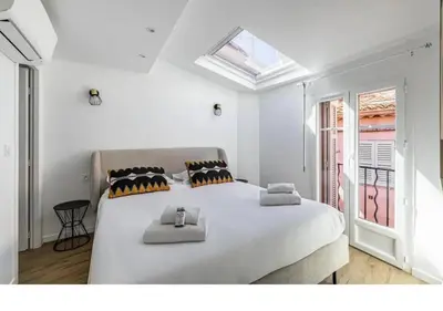 a white bedroom with a large bed and a window at Bright Apartment Mezzanine in the Heart of Suquet in Cannes
