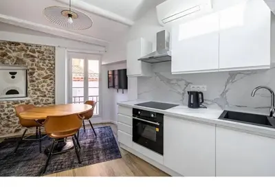 a kitchen with white cabinets and a table and a sink at Bright Apartment Mezzanine in the Heart of Suquet in Cannes