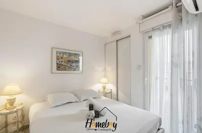 a white bedroom with a bed and a window at Le Palazzio in Cannes