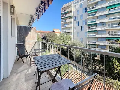 a balcony with a wooden table and benches on a building at Superbe appartement meublé Cannes centre in Cannes