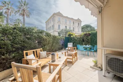 a patio with wooden chairs and tables and a building at 3P Garden-Level Apartment in a Residence with Pool Close to the Center in Cannes