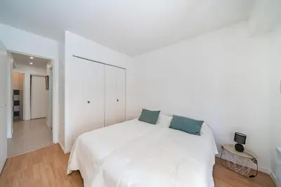 a white bedroom with a white bed with blue pillows at Charmant appartement 2 pièces in Cannes
