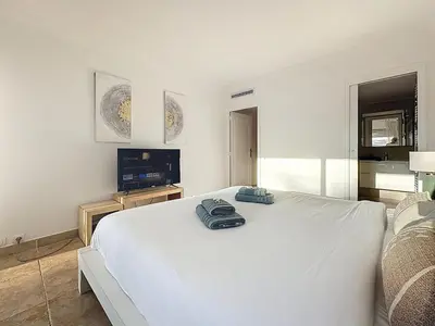 a white bedroom with a large white bed and a television at 86m2, spacieux, 2 chambres, à 1 min de la plage in Cannes