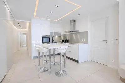 a white kitchen with stools and a counter top at Celestre Croisette - Appartement de Luxe Croisette avec Terrasse et Vue Mer in Cannes