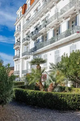 a large white building with palm trees in front of it at Louison balcony, quiet area, 7mn from beach in Cannes