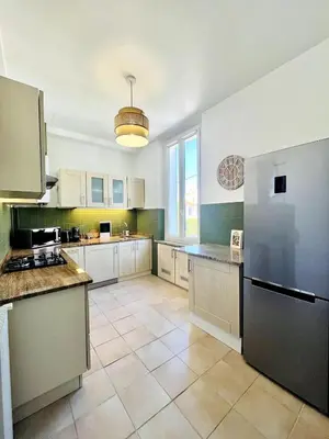 a large kitchen with white cabinets and a large refrigerator at Appartement Calme Proche Plages in Cannes