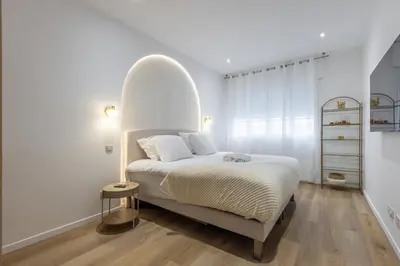 a white bedroom with a bed with an arch overhead at LB Vacation Rentals I Fully Renovated Apt Min from Palais - Beach in Cannes