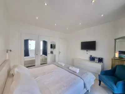 a white bedroom with a large bed and a blue chair at Velasquez Martinez Plage in Cannes