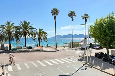 a group of people crossing a street at a crosswalk with palm trees at One-bedroom apt ideally located in front of the Midi beaches in Cannes