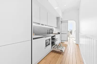 a white kitchen with white cabinets and a wooden floor at Riviera signature apartment by Welcome to Cannes in Cannes