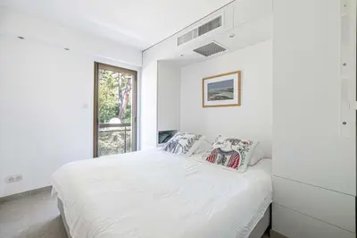 a white bedroom with a bed and a window at LE PARADIS avec deux terrasses équipées et piscine in Cannes