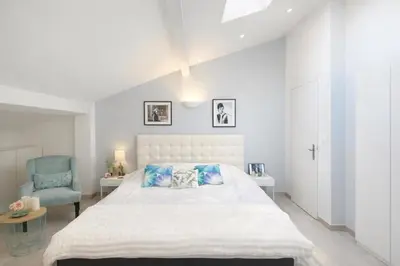 a white bedroom with a bed and a chair at Cozystay 1825 Luxury Duplex on Rue dAntibes in Cannes