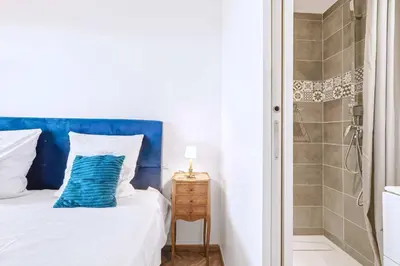 a white bed with a blue headboard and a shower at Jardin Suquet - Appartement panoramique Grande terrasse vue sur mer & Palais in Cannes