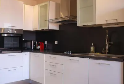 a kitchen with white cabinets and a black wall at SUITE DE LUXE VERVEINE 4P in Cannes