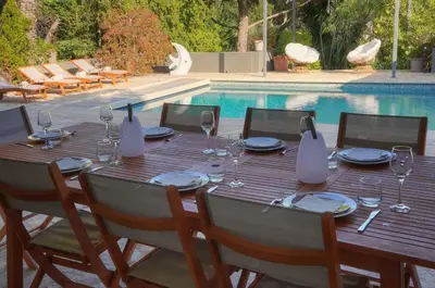 a wooden table with wine glasses and plates next to a pool at Villa Lou Bayou French Riviera near Cannes in Vallauris