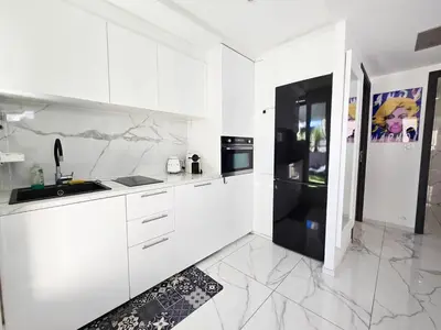 a white kitchen with white cabinets and a black refrigerator at 51m2 Gray d'Albion, Croisette, terrasse & clim in Cannes