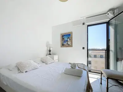 a white bedroom with a bed and a large window at Appartement 3 pièces à Cannes avec piscine in Cannes
