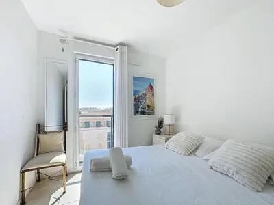 a white bedroom with a bed and a window at Appartement 3 pièces à Cannes avec piscine in Cannes