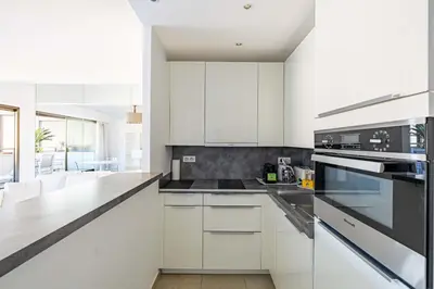 a kitchen with white cabinets and black appliances at 64 ANTIBES - Stunning 1-bedroom with terrace at Gray d'Albion in Cannes