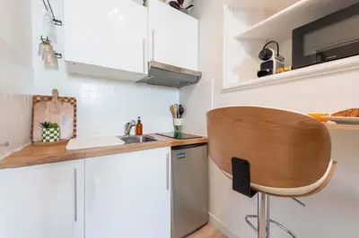 a kitchen with white cabinets and a wooden chair at Studio design au centre de Cannes proche Croisette climatisé in Cannes