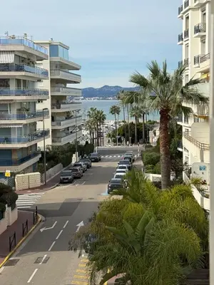 a street with parked cars and palm trees next to buildings at Spacious 2-bedroom sea view with parking in Palm Beach in Cannes