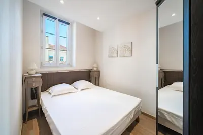 a white bedroom with a bed and a window at Cozystay 1802 One bedroom in the Heart of Cannes in Cannes