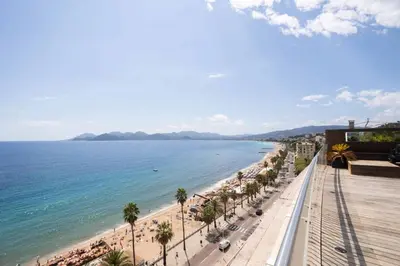 a view of a beach with palm trees and the ocean at REF 2043 - Cannes Penthouse with panoramic sea view for rent in Cannes