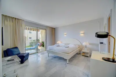 a white bedroom with a bed and a blue chair at IMMOGROOM- Huge Terrace - Panoramic Sea View - 1min from Beach in Cannes