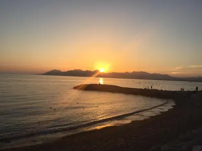 a sunset on a beach with the sun setting over the ocean at Studio Cosy Merle in Cannes