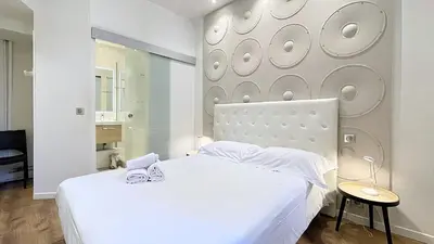 a white bedroom with a large white bed and a mirror at Hotel Le Florian in Cannes