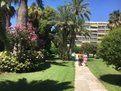 two people walking down a path in a park with palm trees at Sea Side apartment in Cannes
