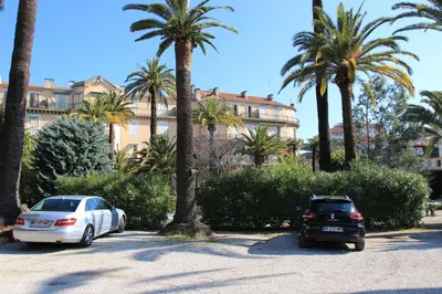 two cars parked in a parking lot with palm trees at Le Pavillon113 in Cannes