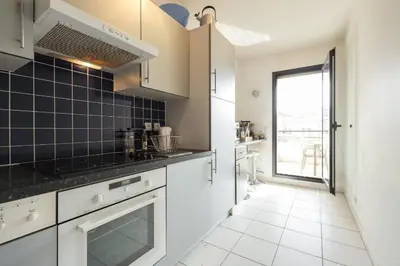 a kitchen with white cabinets and black tiles on the wall at Appartement de charme à Cannes + terrasse in Cannes
