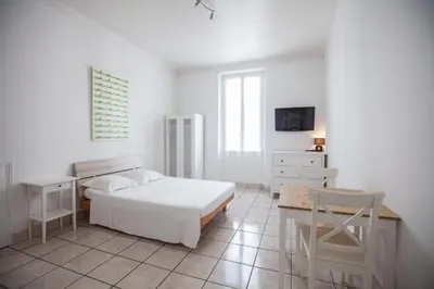 a white bedroom with a bed and a desk and a chair at Appartements Foch in Cannes