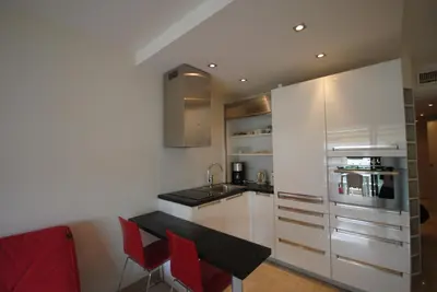 a kitchen with white cabinets and a table and red chairs at Résidence Gray d'Albion 2P NAP558 in Cannes